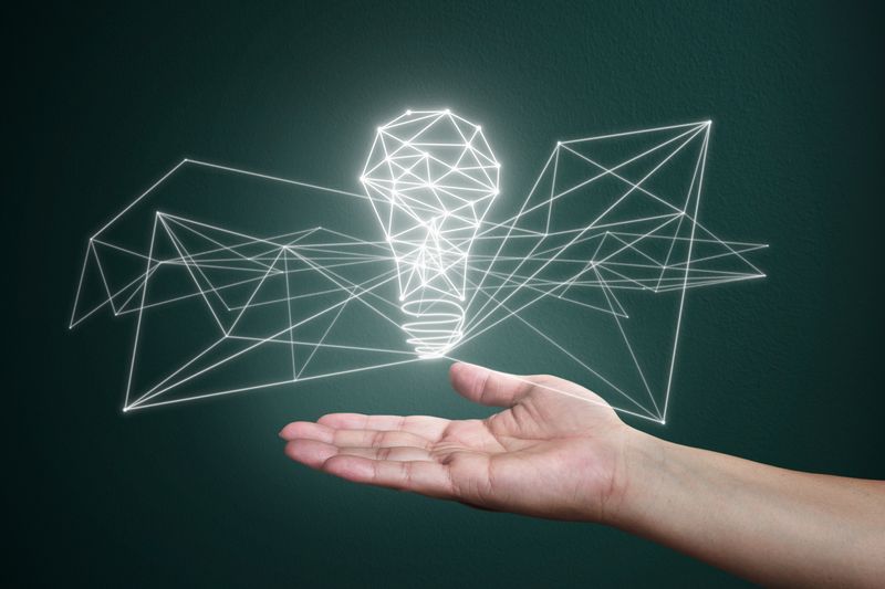 BTveriBDeG_Dhn75PWLN- - Prodify Digital Hand beneath a glowing wireframe light bulb made of geometric lines, symbolizing ideas and innovation.