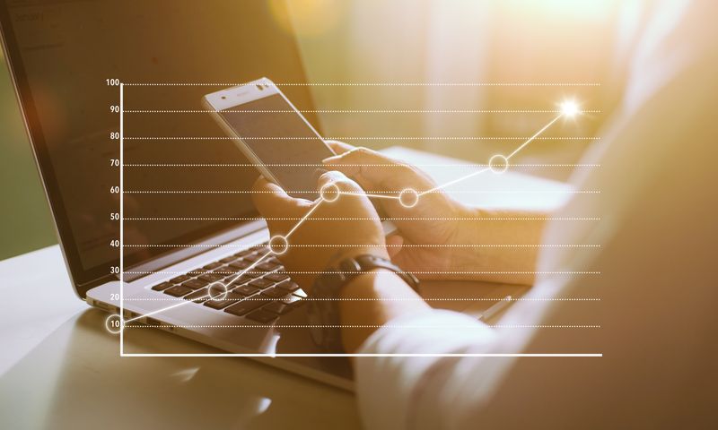 Hands typing on a laptop while holding a smartphone, with a white rising line chart overlay showing growth.