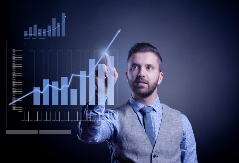nKpMcXQ3Ok2Jb5MoMic01 - Prodify Digital Businessman in a vest points at glowing, upward-trending charts on a transparent dashboard.