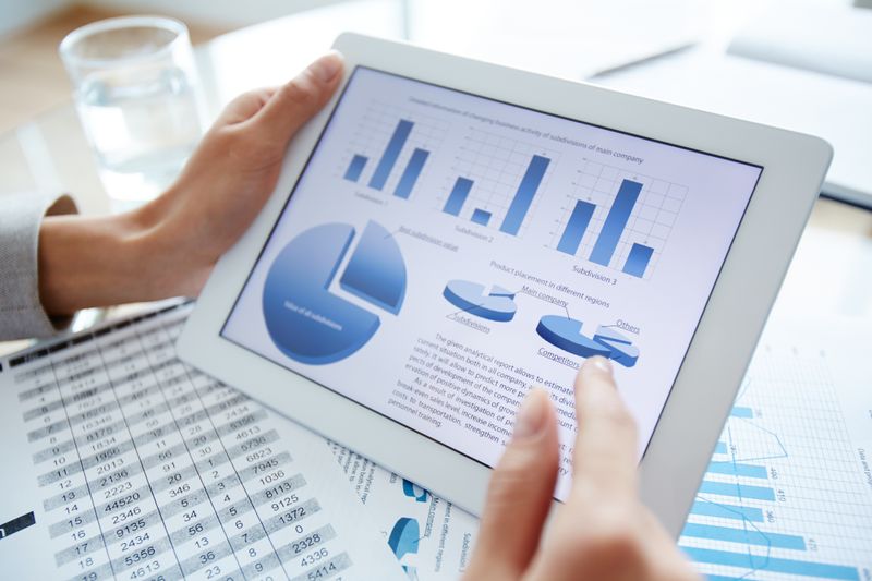 yV3NGKCQCHKy4ZniDO8P9 - Prodify Digital Hands hold a tablet displaying bar and pie charts with data sheets in the background.
